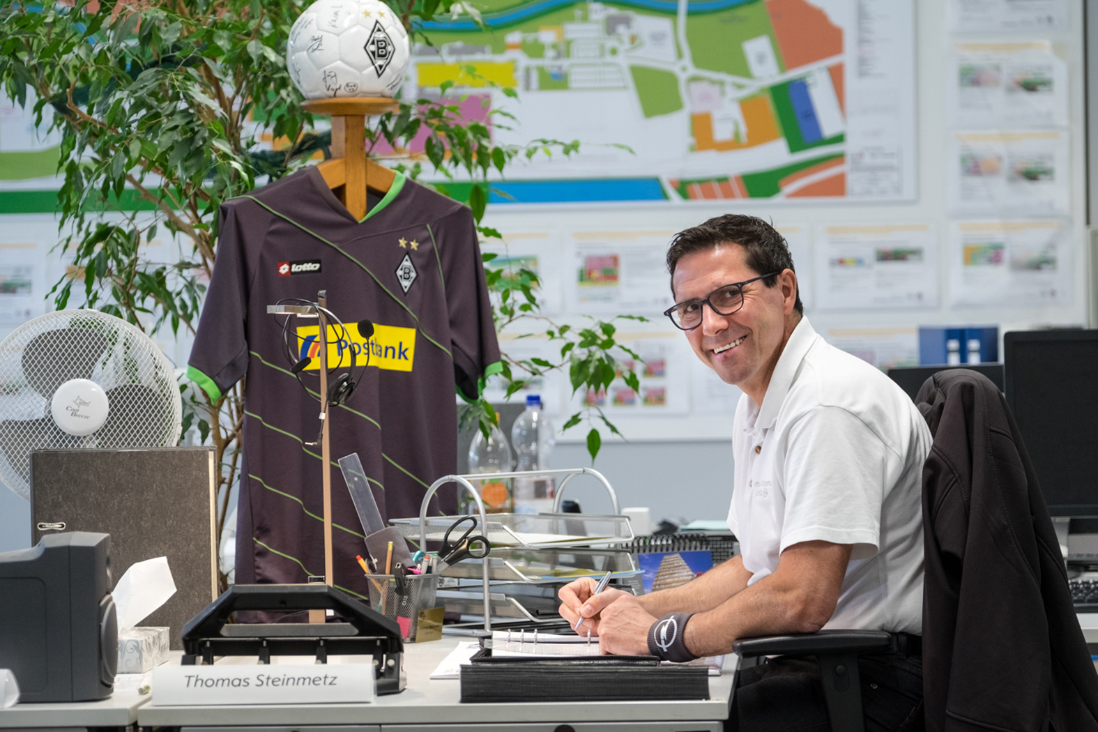 Thomas Steinmetz an seinem Büro-Arbeitsplatz. Im Hintergrund ein Geschenk der Kollegen, das eindeutig zeigt, für welchen Fußballverein sein Herz schlägt – Borussia Mönchengladbach